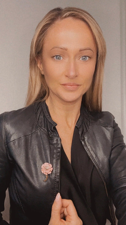 A pink enamelled flower brooch with a diamond centre, in yellow gold, modelled by a woman wearing a black jacket