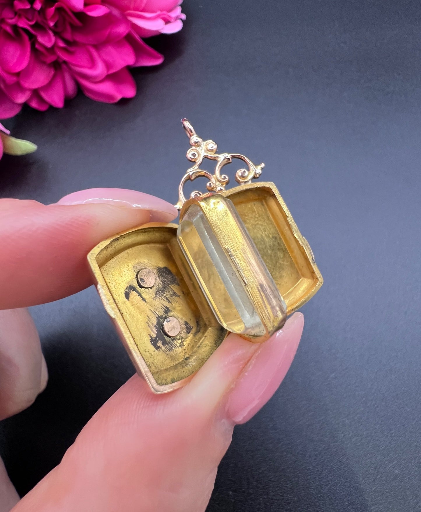 A yellow gold ornate locket with diamond fleur-de-lis detail, open, held in a hand