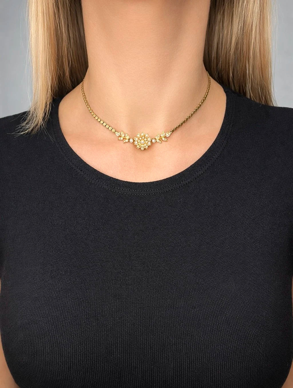 A yellow gold pearl floral necklace with integrated chain, modelled by a woman wearing a black top