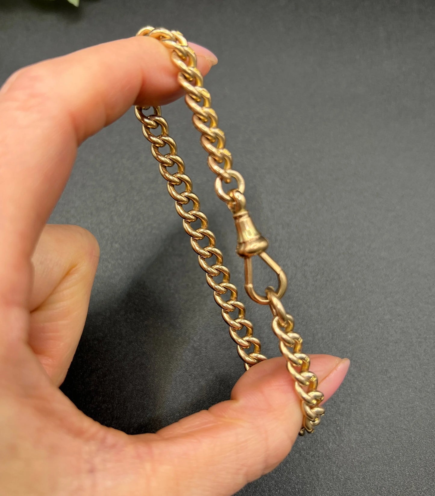 A gold curb link bracelet with a lobster claw clasp, held in a hand