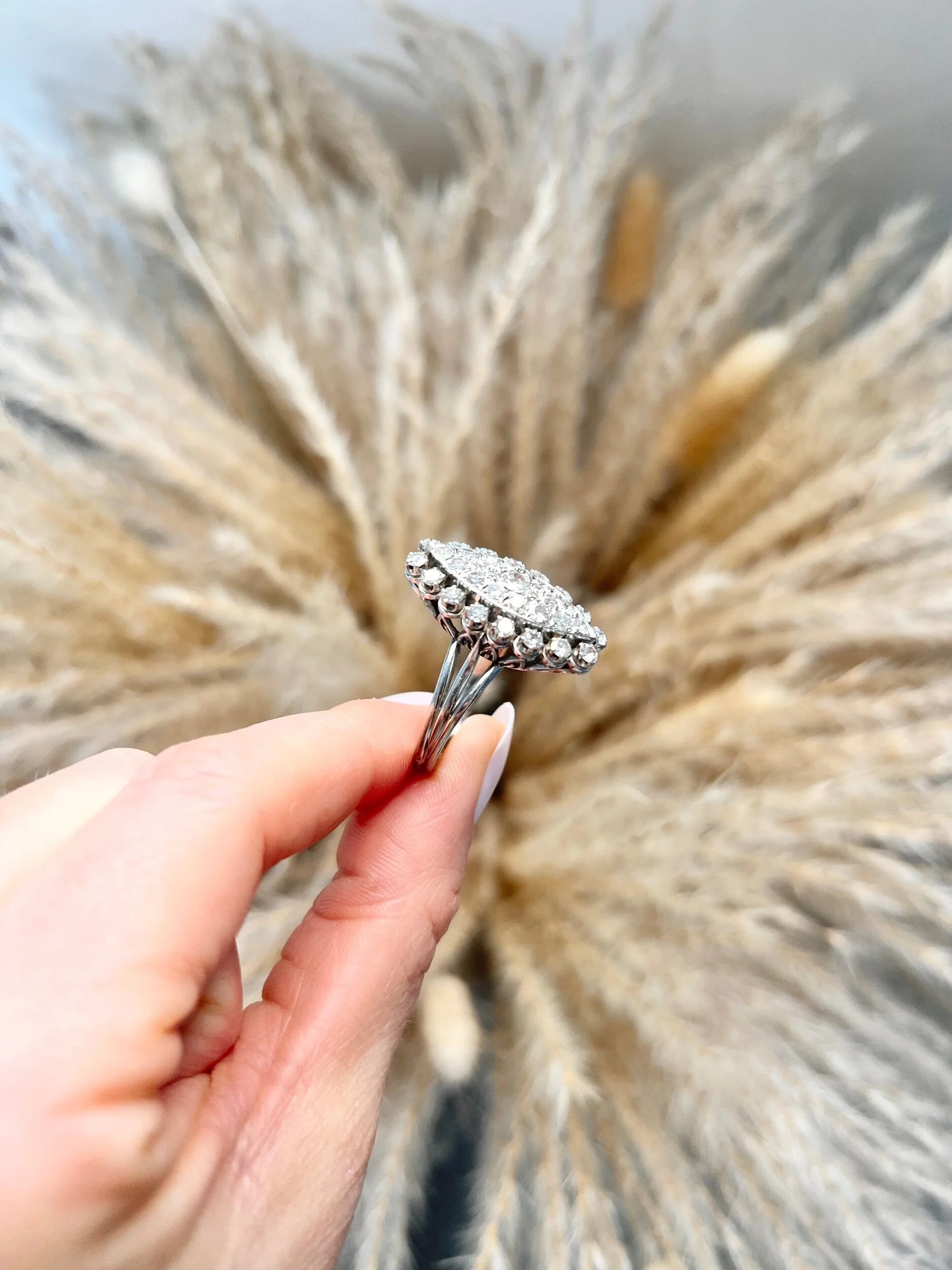 A navette shaped diamond cluster ring in white metal, held in a hand
