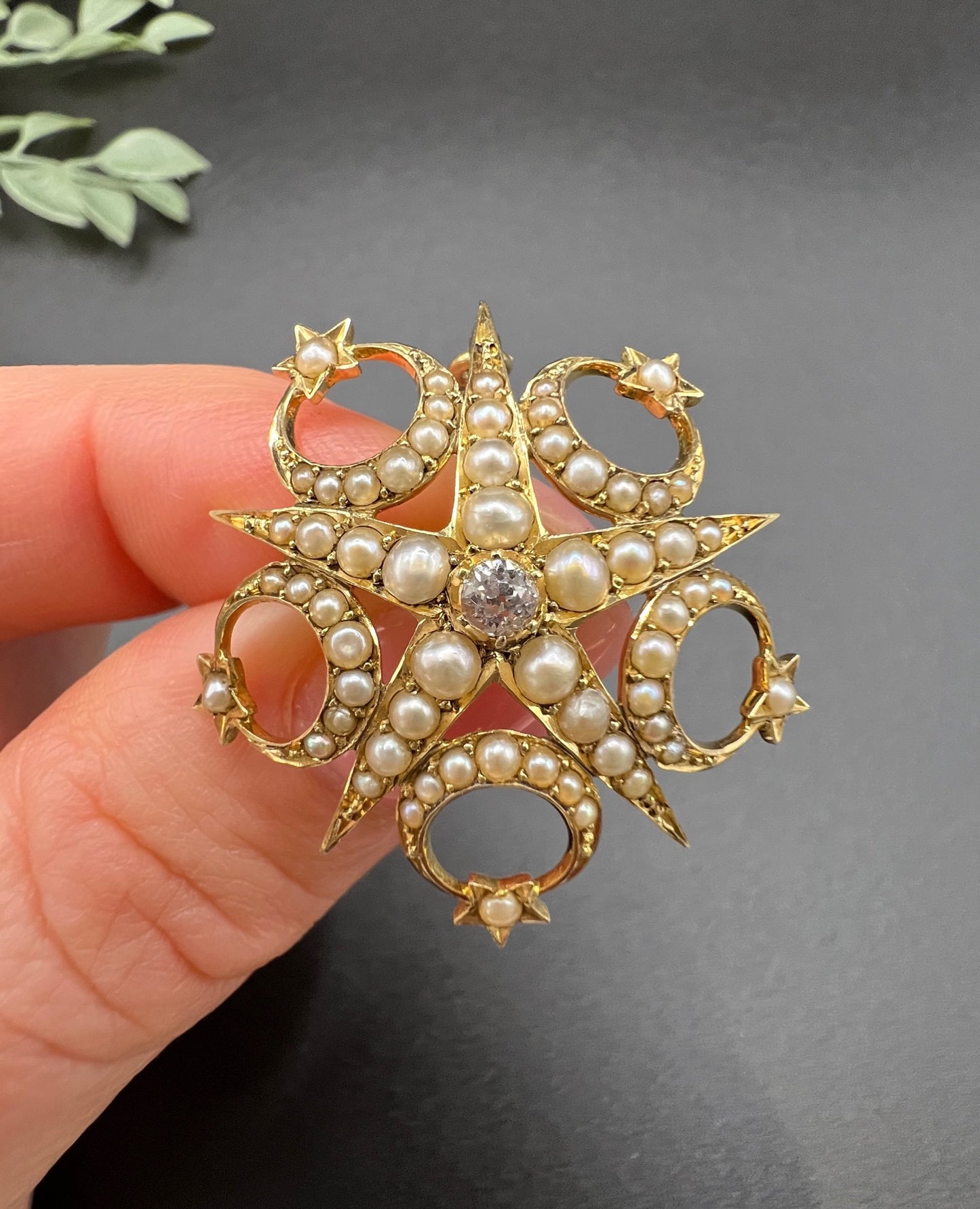 A yellow gold star and crescent brooch/pendant set with a diamond and pearls, held in a hand