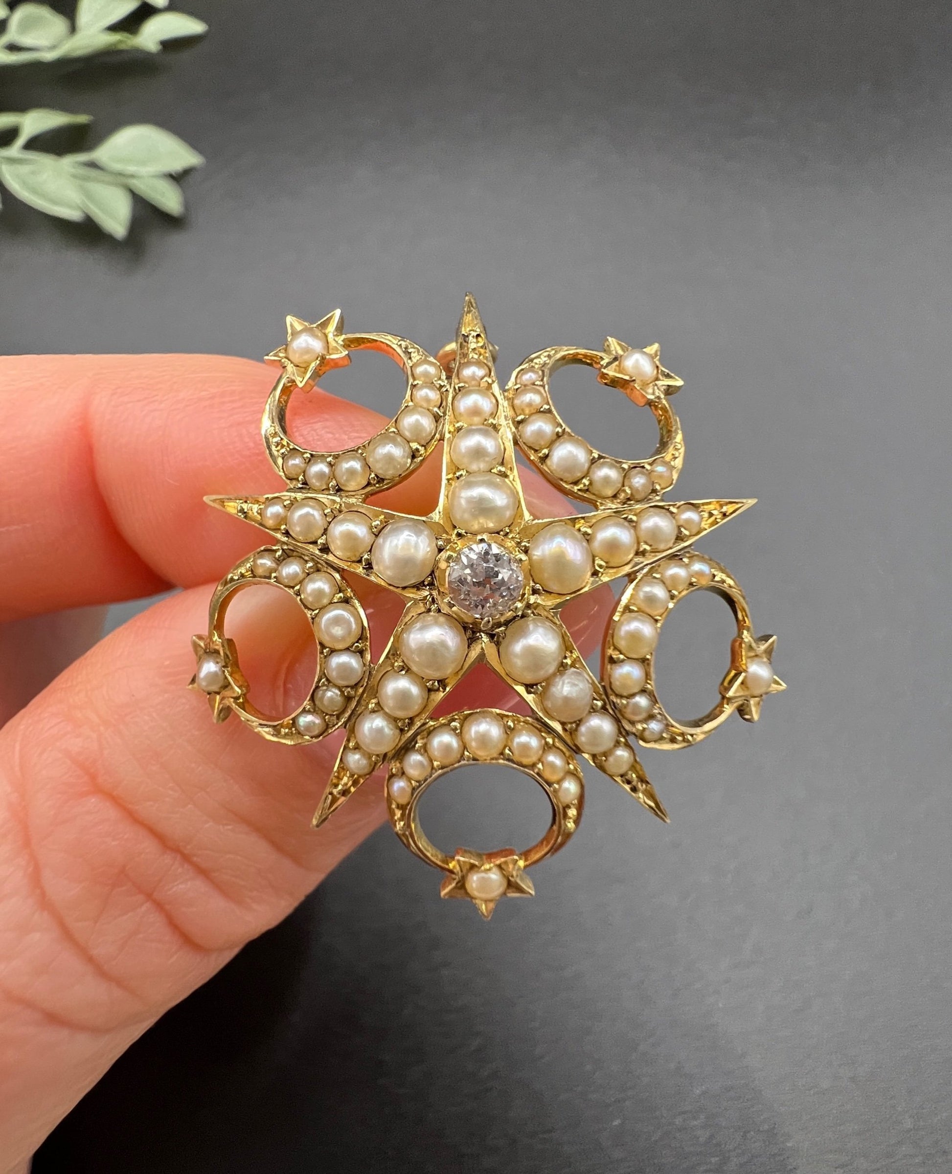 A yellow gold star and crescent brooch/pendant set with a diamond and pearls, held in a hand