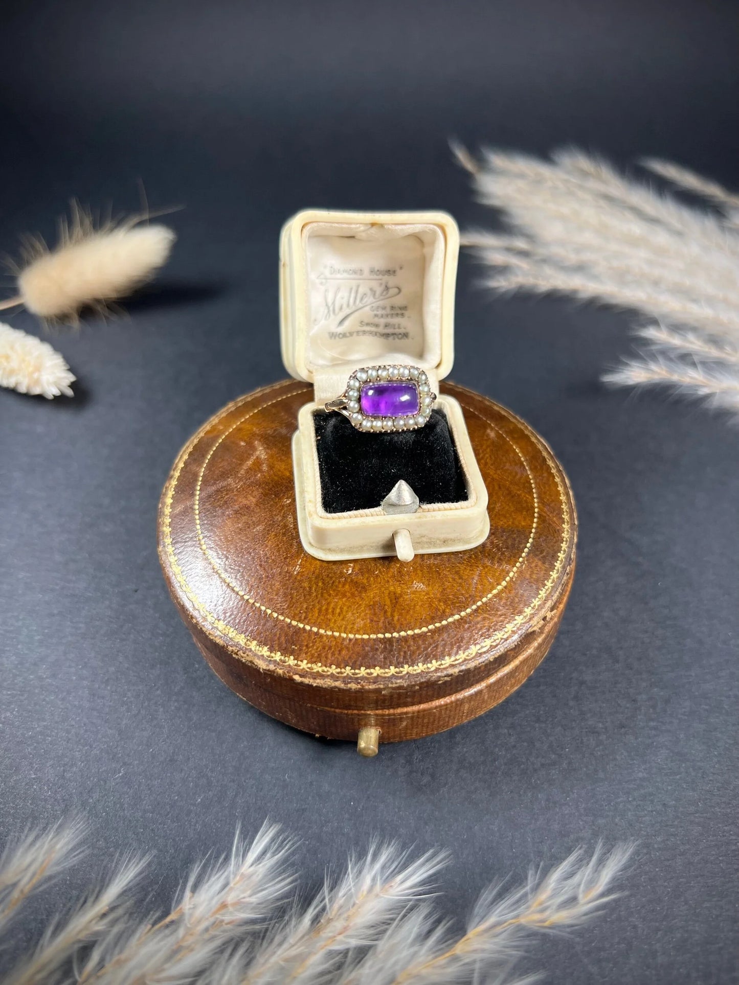 A cabochon amethyst and pearl halo cluster ring in gold, in a ring box