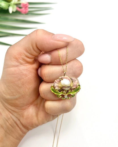 An enamel, diamond and pearl flower pendant with a gold chain, held in a hand