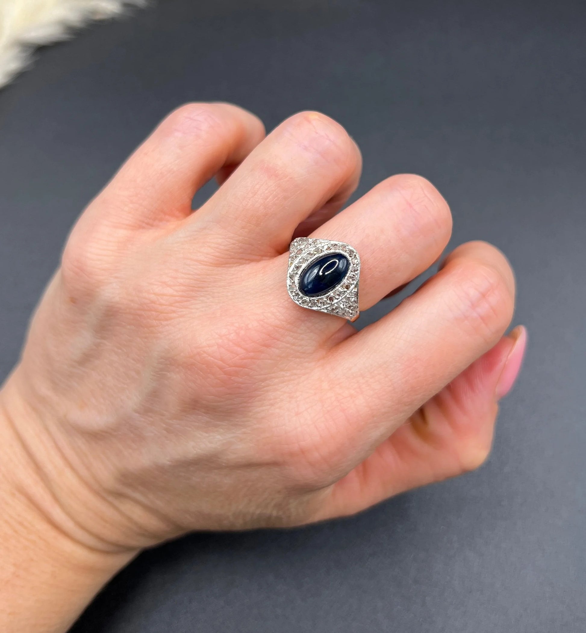 An oval cabochon sapphire and diamond fancy cluster ring in yellow and white gold, modelled on a hand