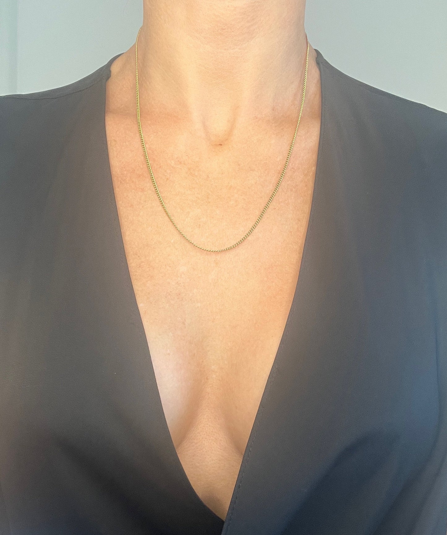 A yellow gold chain necklace, modelled by a woman wearing a black top