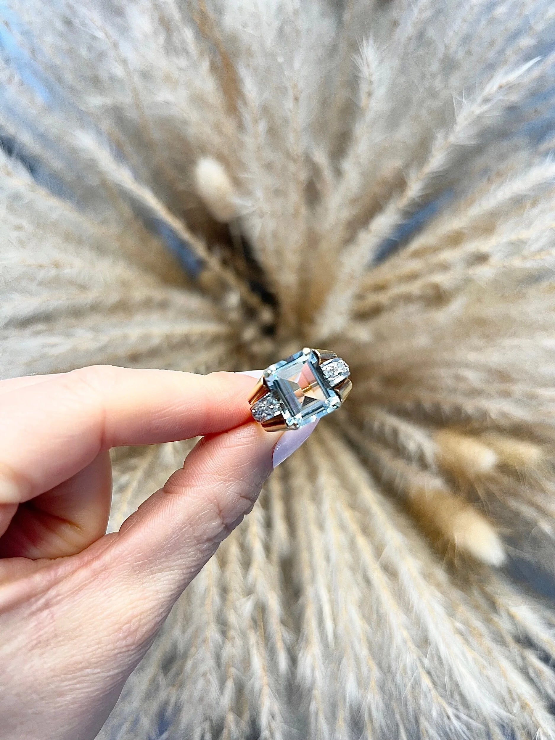 An aquamarine and diamond cocktail ring in gold, held in a hand