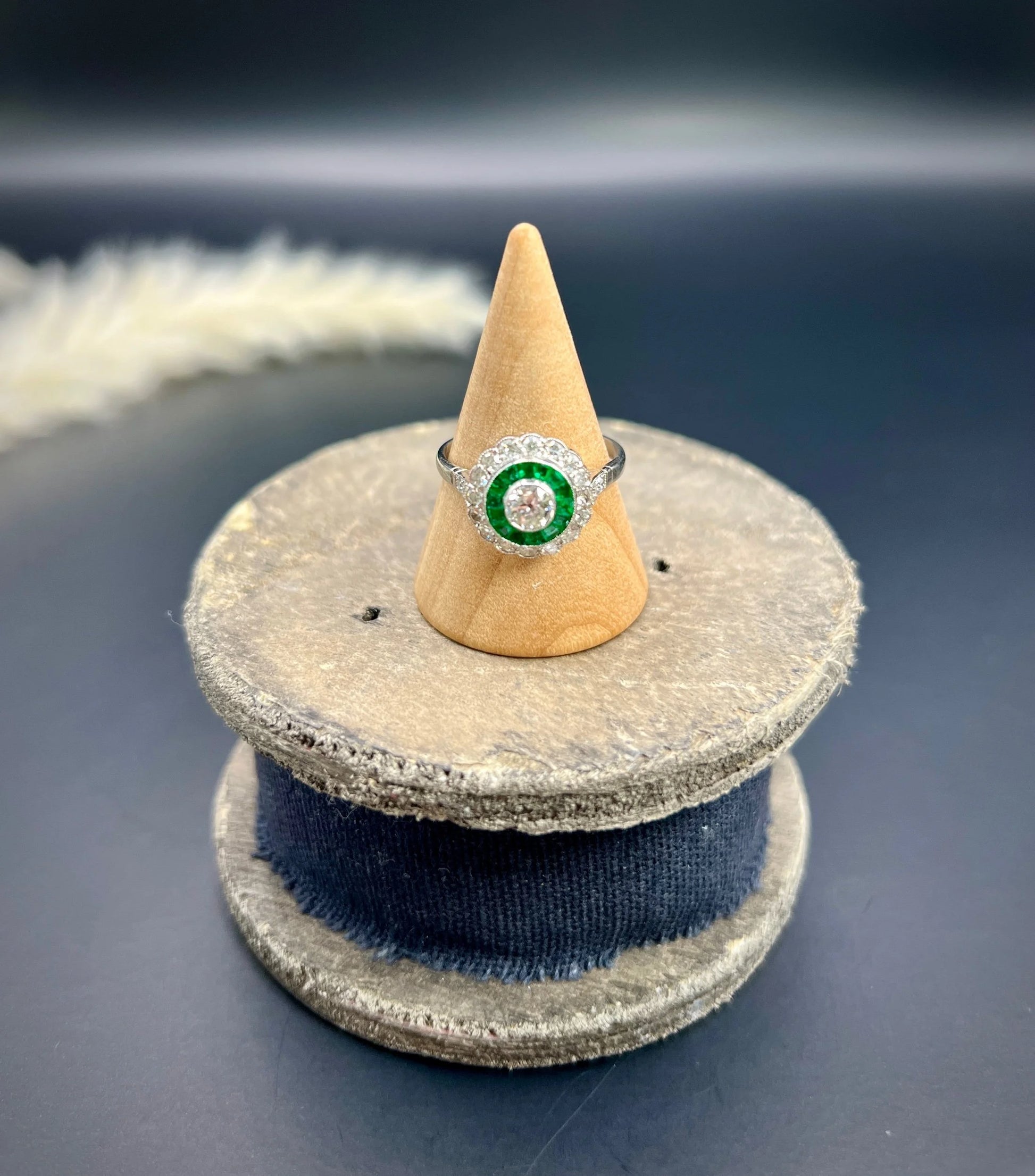 An emerald and diamond target cluster ring in platinum, on a ring cone