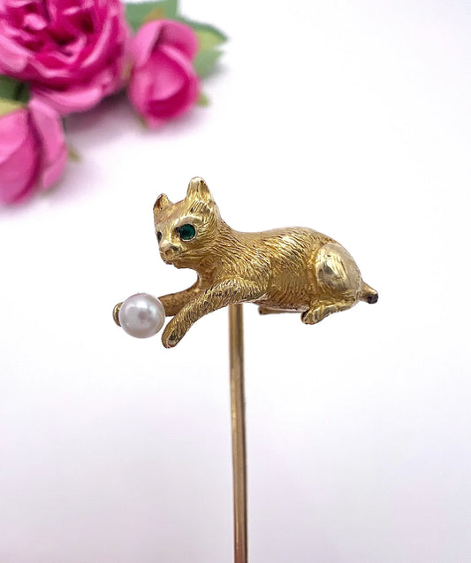 A yellow gold cat playing with a pearl ball stick pin