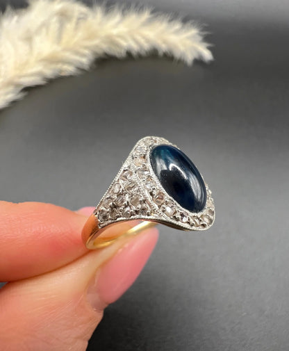 An oval cabochon sapphire and diamond fancy cluster ring in yellow and white gold, held in a hand