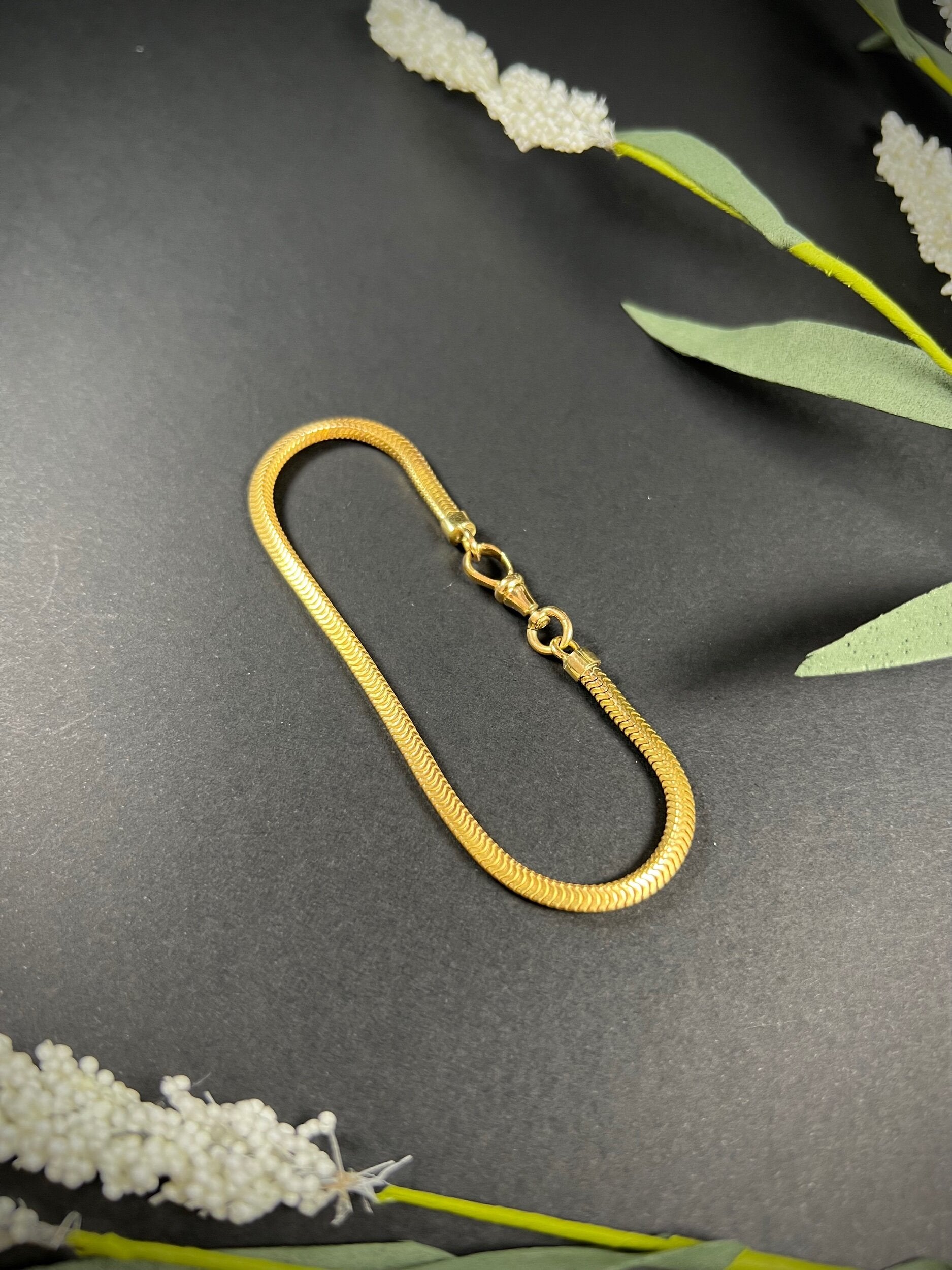 A yellow gold snake link bracelet, laid flat on a black background
