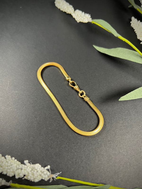 A yellow gold snake link bracelet, laid flat on a black background