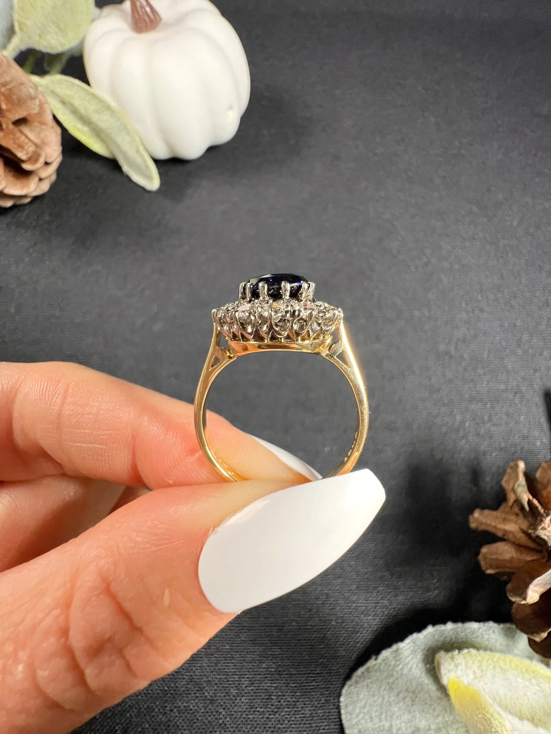 A round sapphire and diamond cluster ring, held in a hand