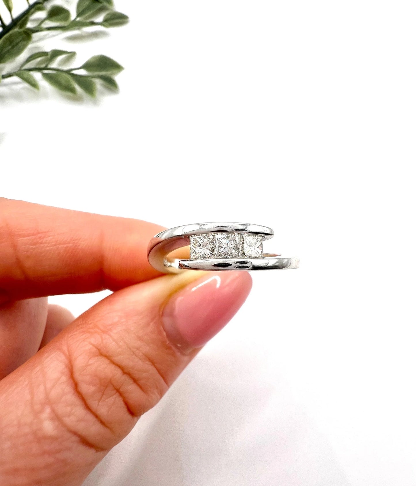 A three stone princess cut diamond crossover ring in white gold, held in a hand