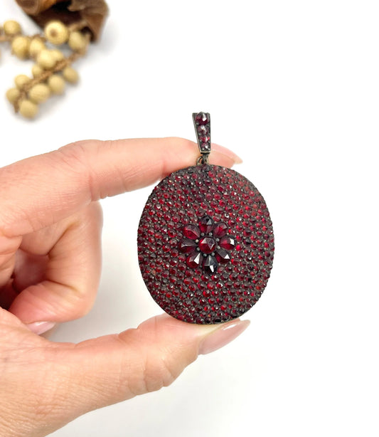An antique oval locket encrusted with garnets, held in a hand