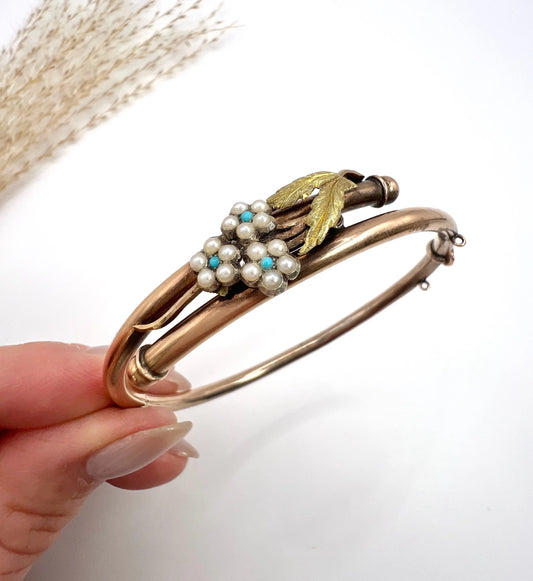 A rose and yellow gold floral bangle bracelet with turquoise and pearls, held in a hand