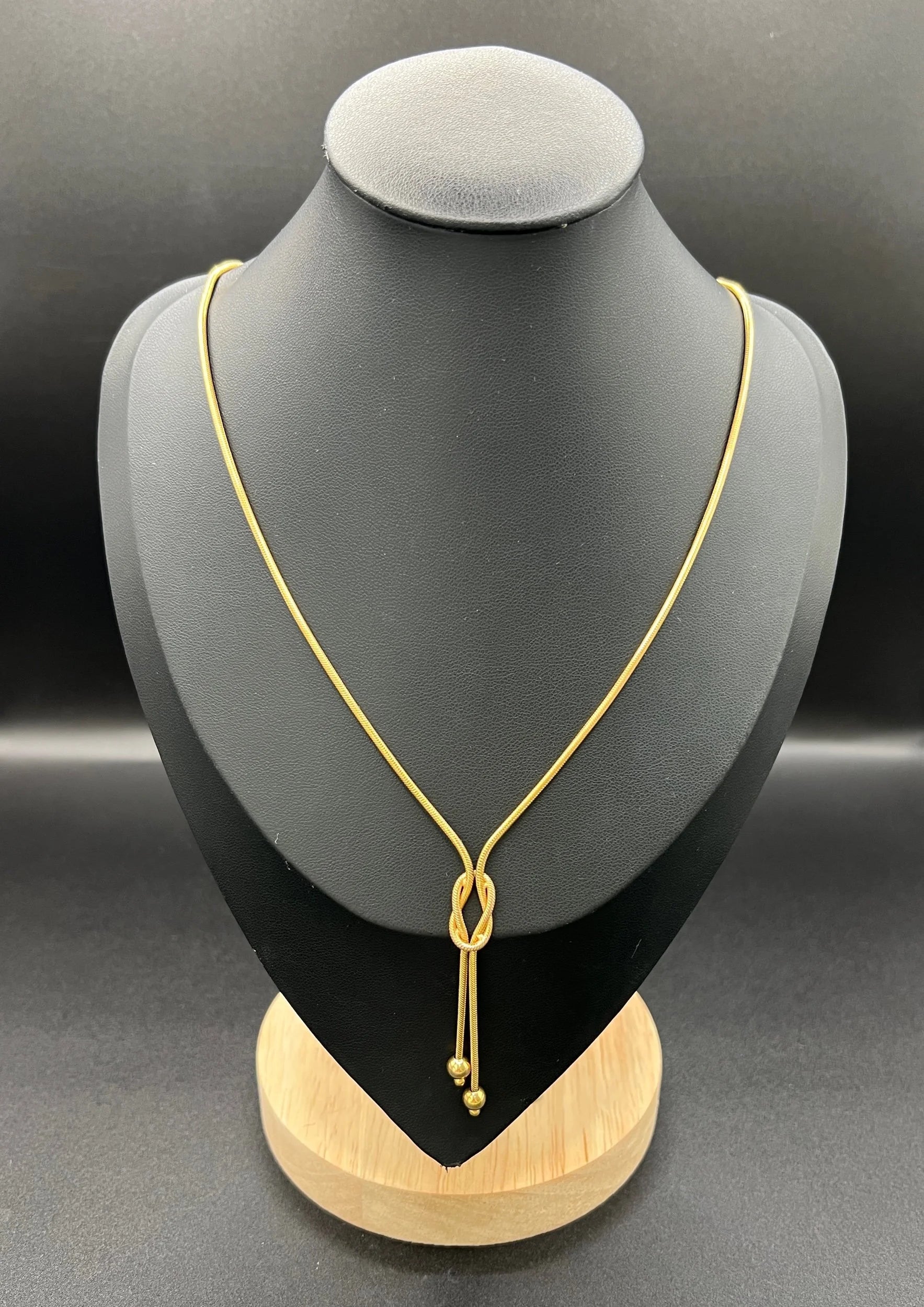A yellow gold snake link chain necklace with a knot and tassel drop, on a black bust