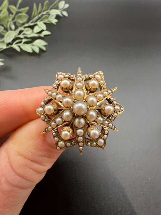 A yellow gold brooch/pendant with pearls in the shape of a star, held in a hand