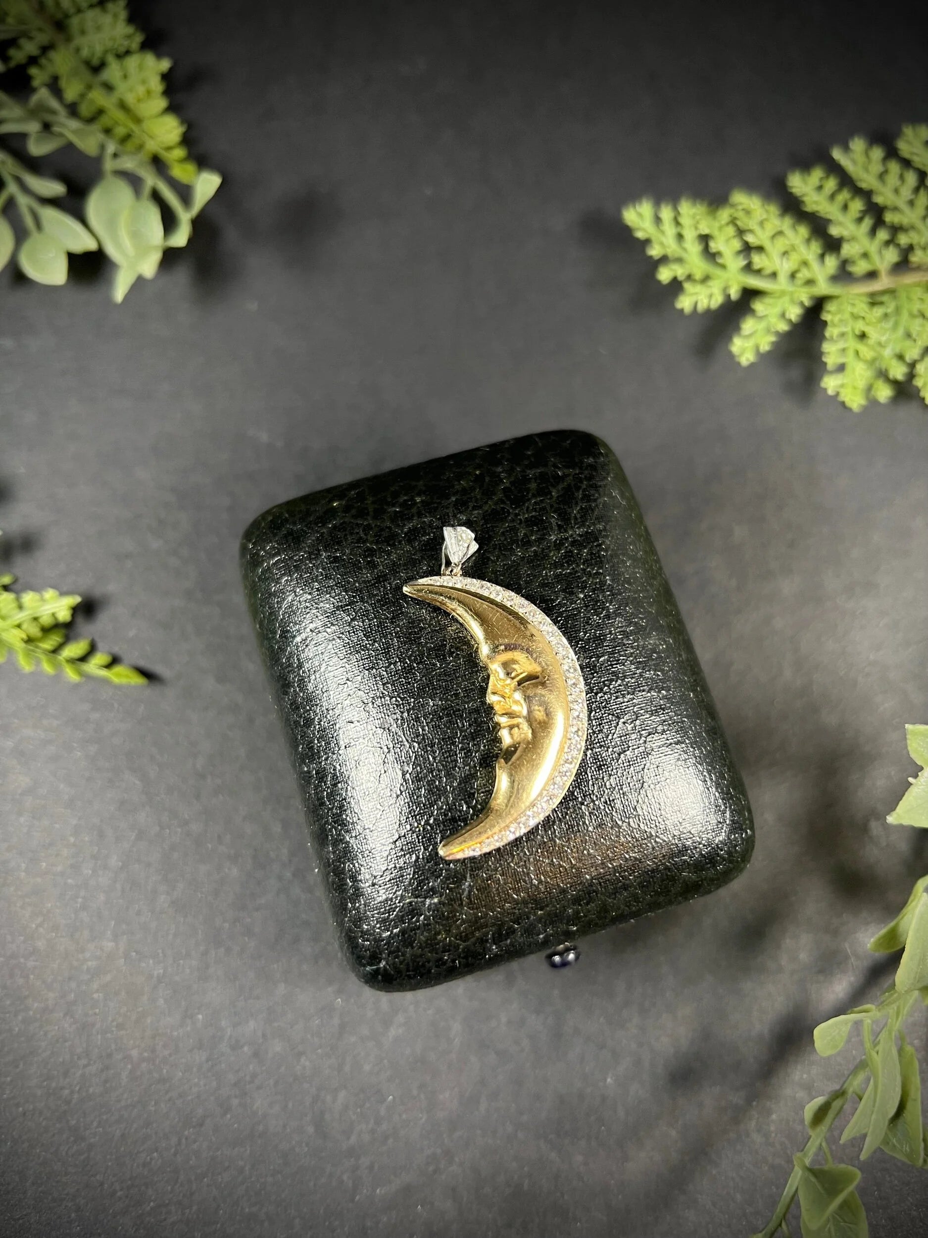 A gold crescent moon pendant with diamonds, on an antique box