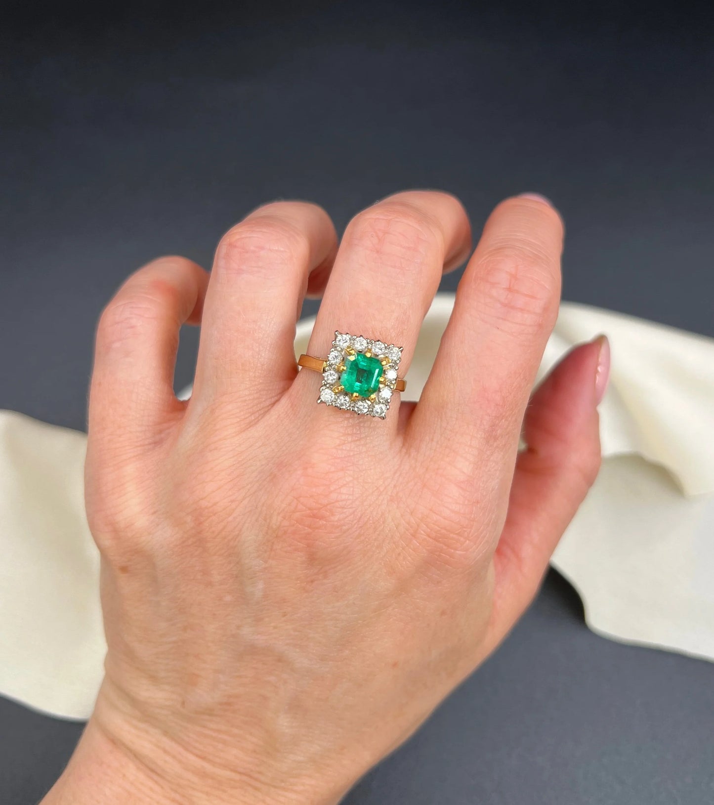 A square shaped emerald and diamond cluster ring in yellow and white gold, modelled on a hand