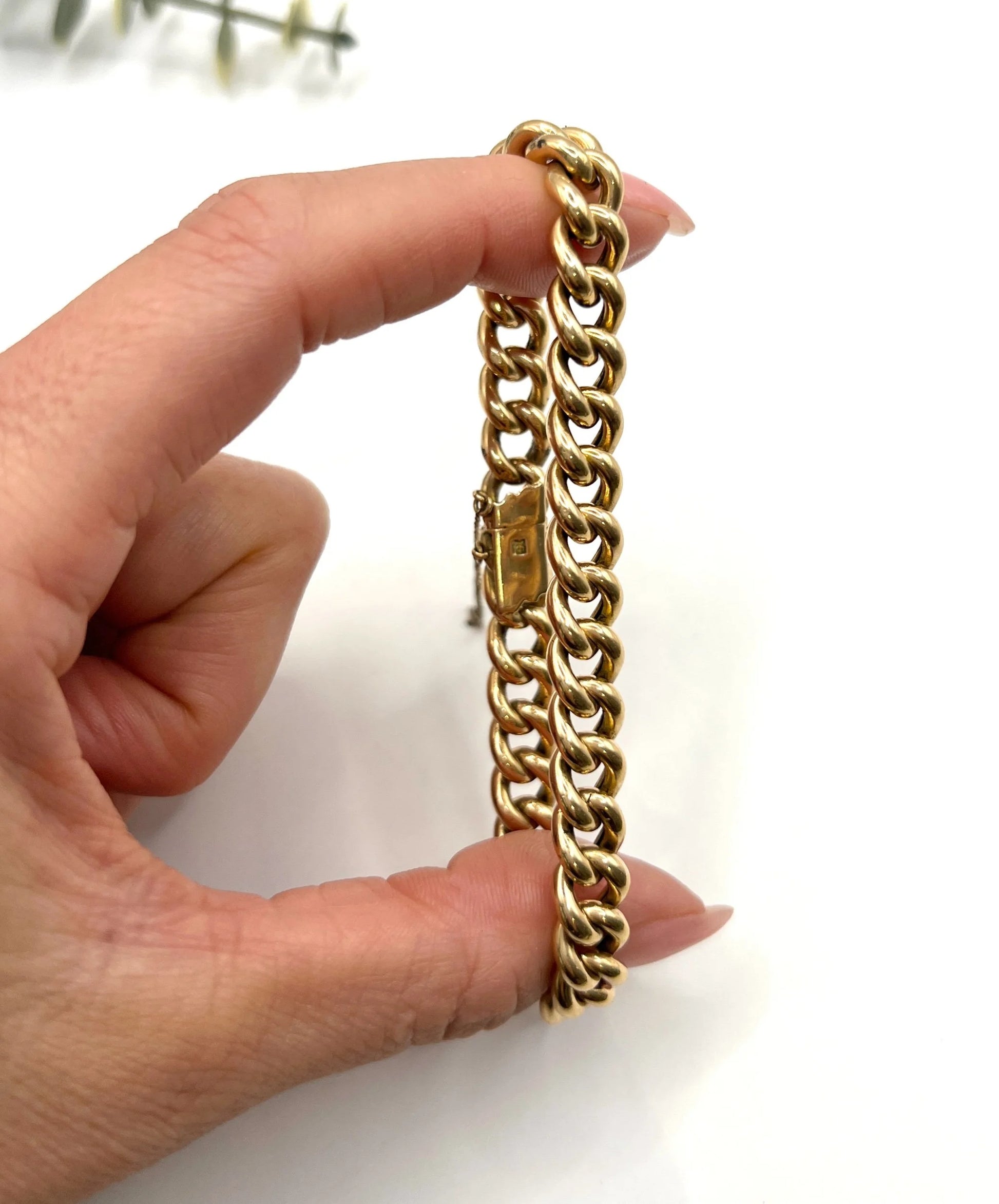 A curb link bracelet in yellow gold, held in a hand