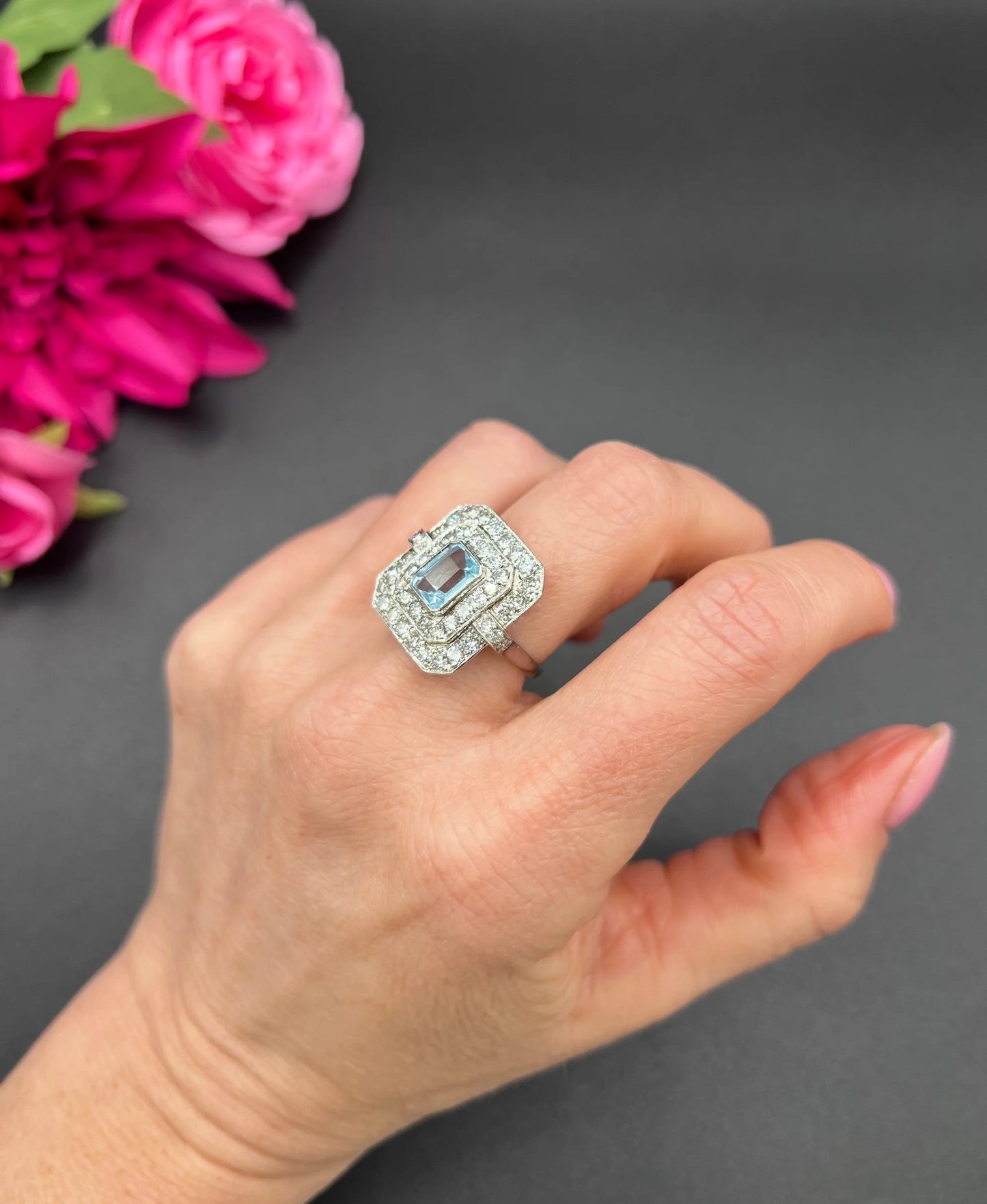 An octagonal shaped cluster ring with an aquamarine centre surrounded by two rows of diamonds, in platinum, modelled on a hand