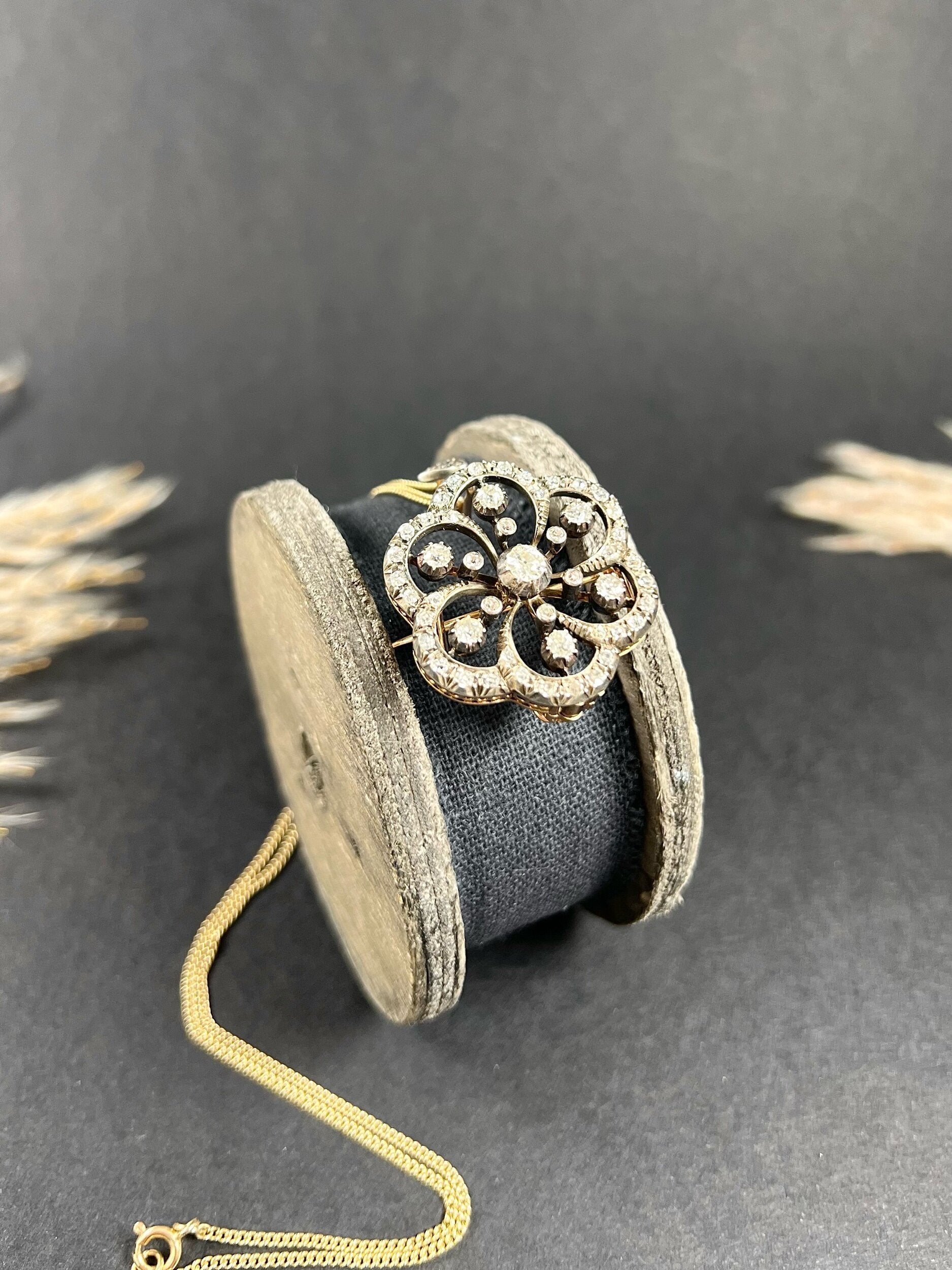 A floral design diamond set pendant/brooch, with a gold chain, on an antique box