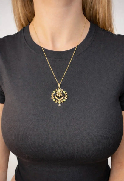A peridot and pearl floral circle brooch/pendant in yellow gold, with a chain, modelled by a woman wearing a black top