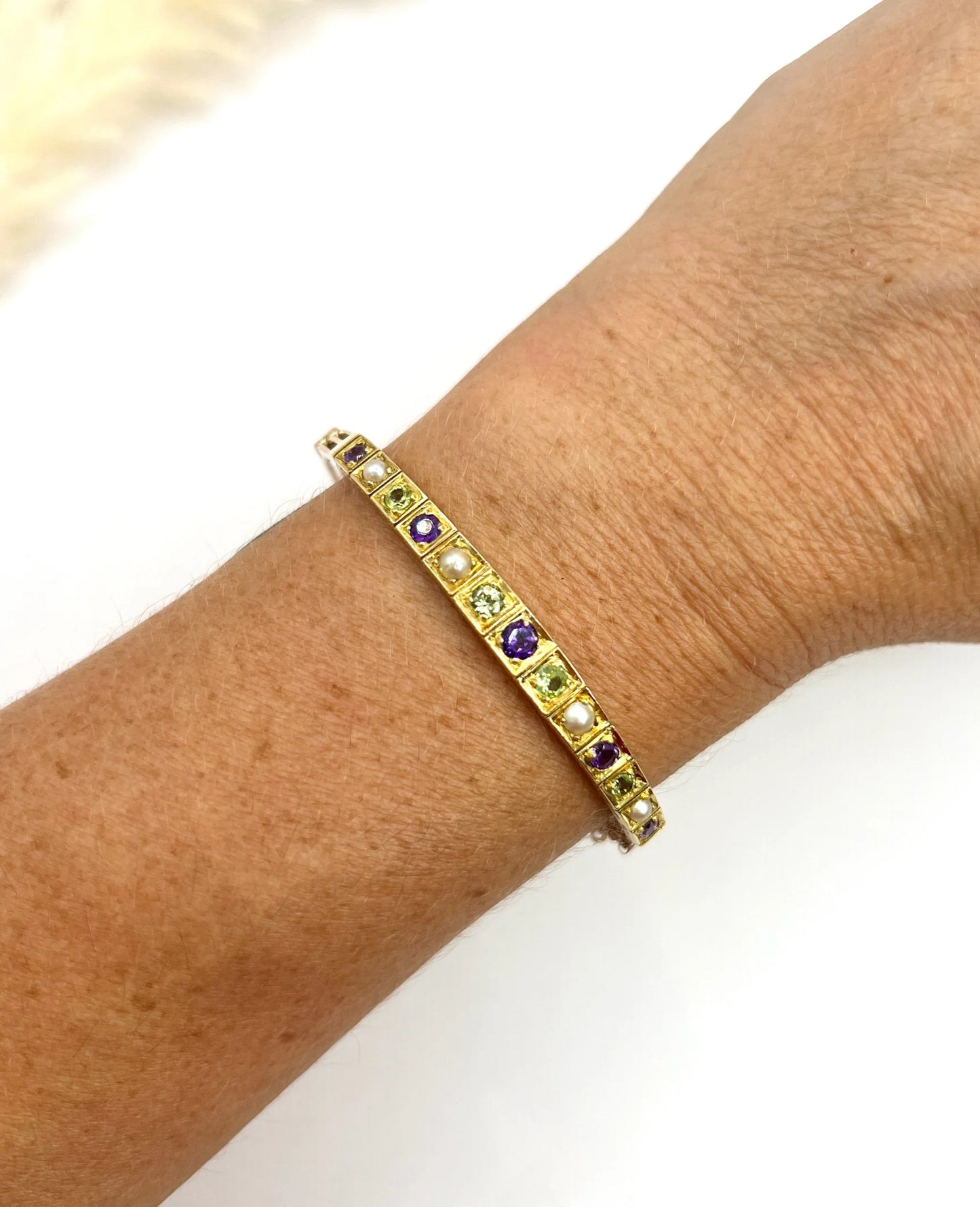 A yellow gold peridot, amethyst and pearl bangle bracelet, modelled on a wrist
