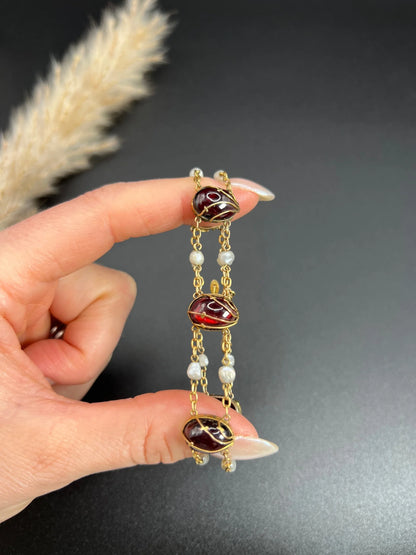 A yellow gold bracelet with oval cabochon garnets and white pearls, in a hand