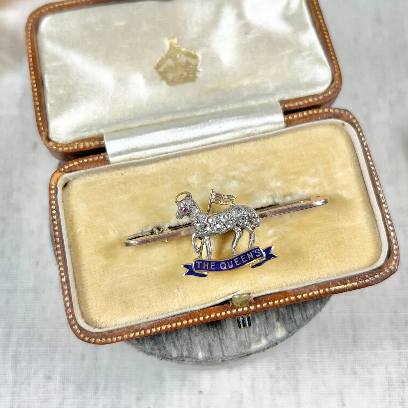 A diamond set regimental bar brooch in gold, with a blue enamel banner reading THE QUEEN'S