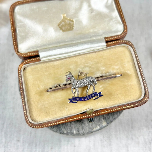 A diamond set regimental bar brooch in gold, with a blue enamel banner reading THE QUEEN'S