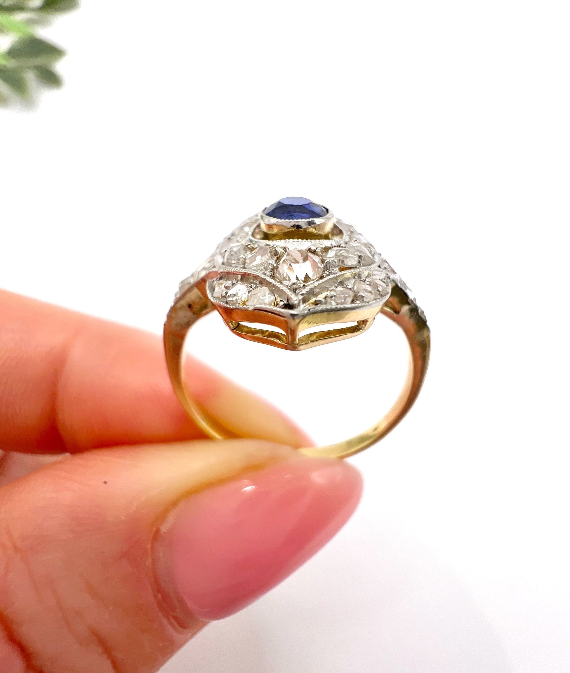 A sapphire and diamond openwork ring in platinum with a yellow gold ring shank, held in a hand
