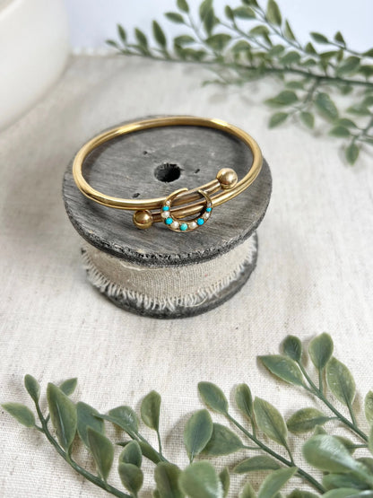 A yellow gold crossover bangle bracelet with a pearl and turquoise crescent moon centre