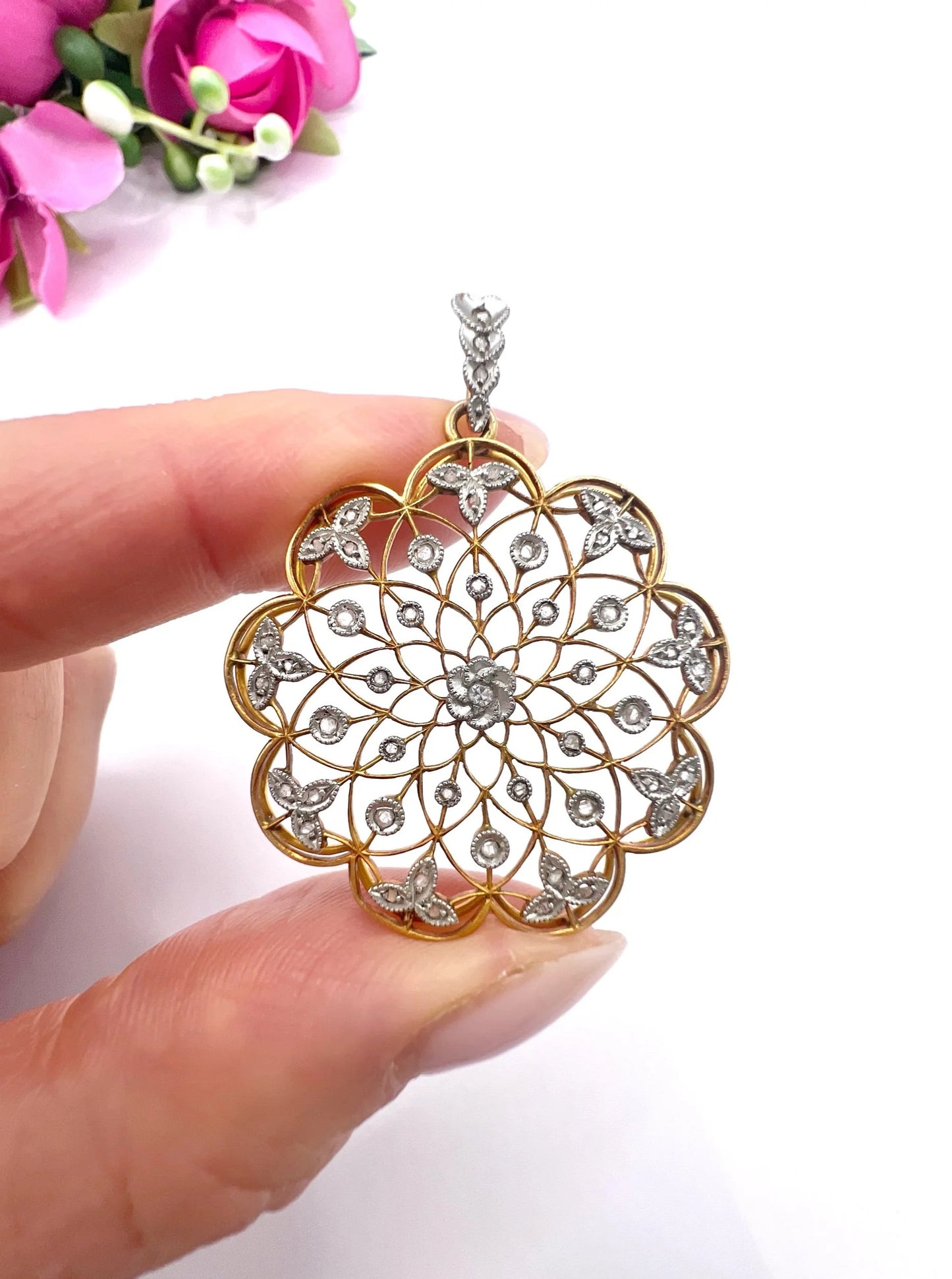 A floral openwork diamond pendant in gold and platinum, held in a hand