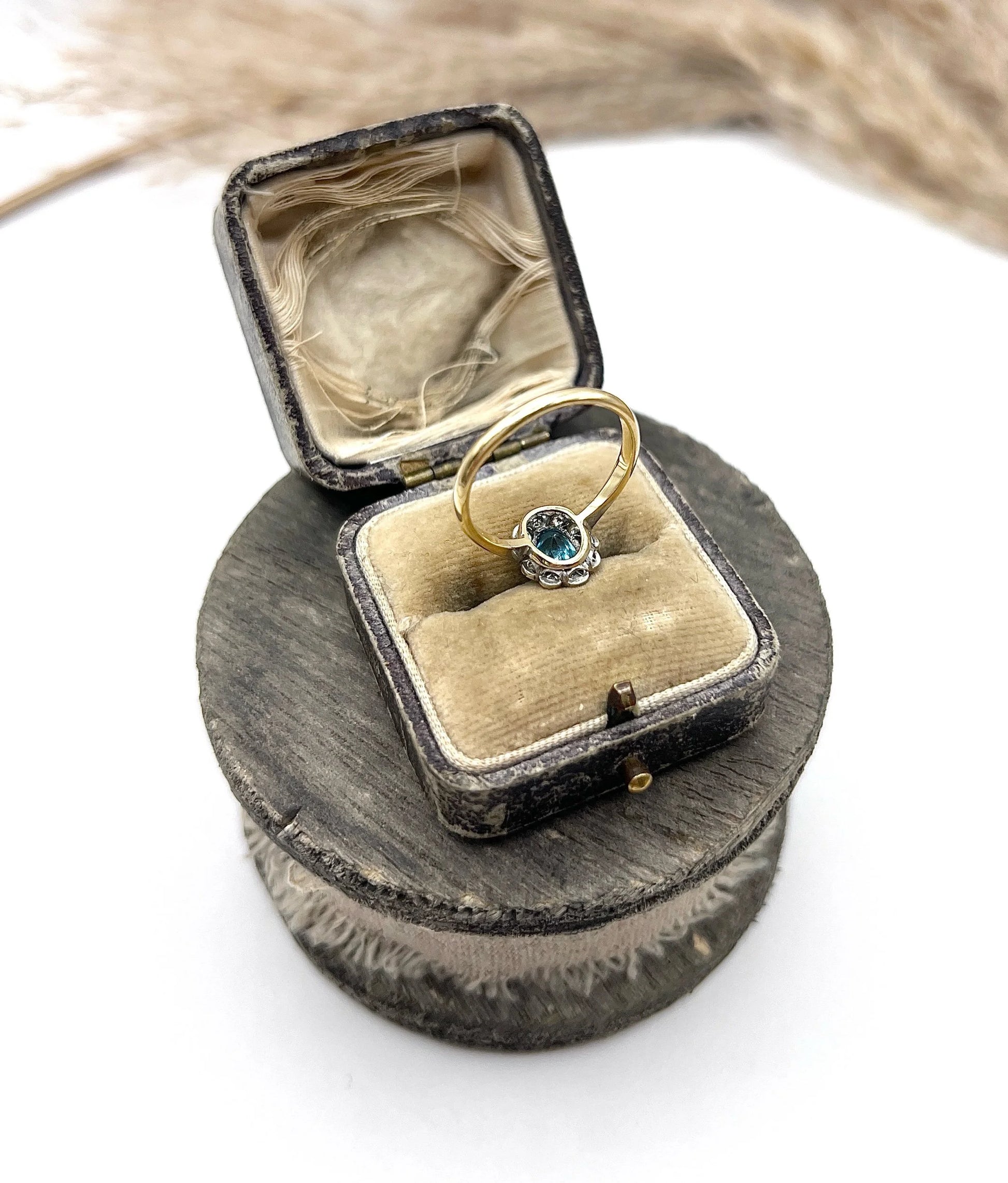 An oval cluster ring with a blue zircon centre surrounded by round diamonds, in yellow gold and platinum, in an antique ring box