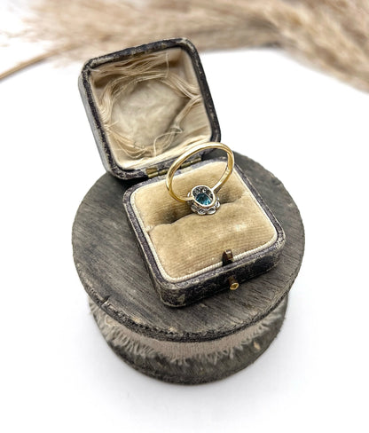 An oval cluster ring with a blue zircon centre surrounded by round diamonds, in yellow gold and platinum, in an antique ring box