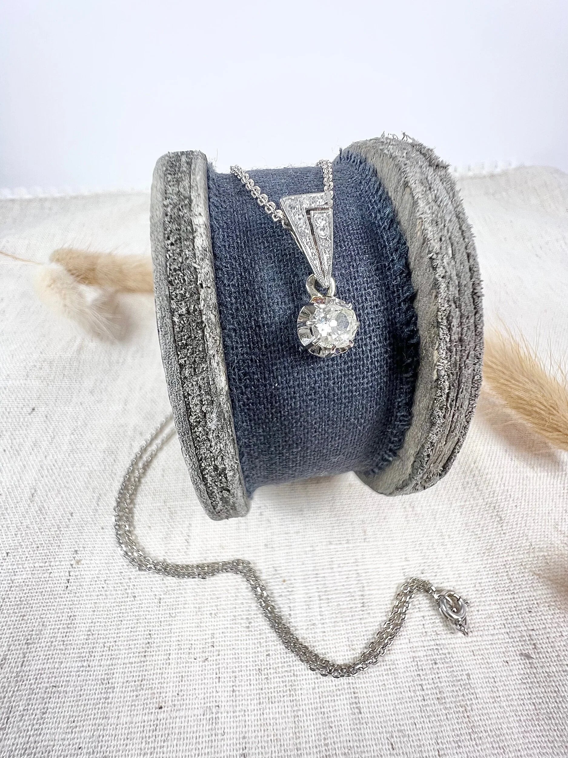 An old cut diamond pendant in white metal with a matching chain, on a circular object