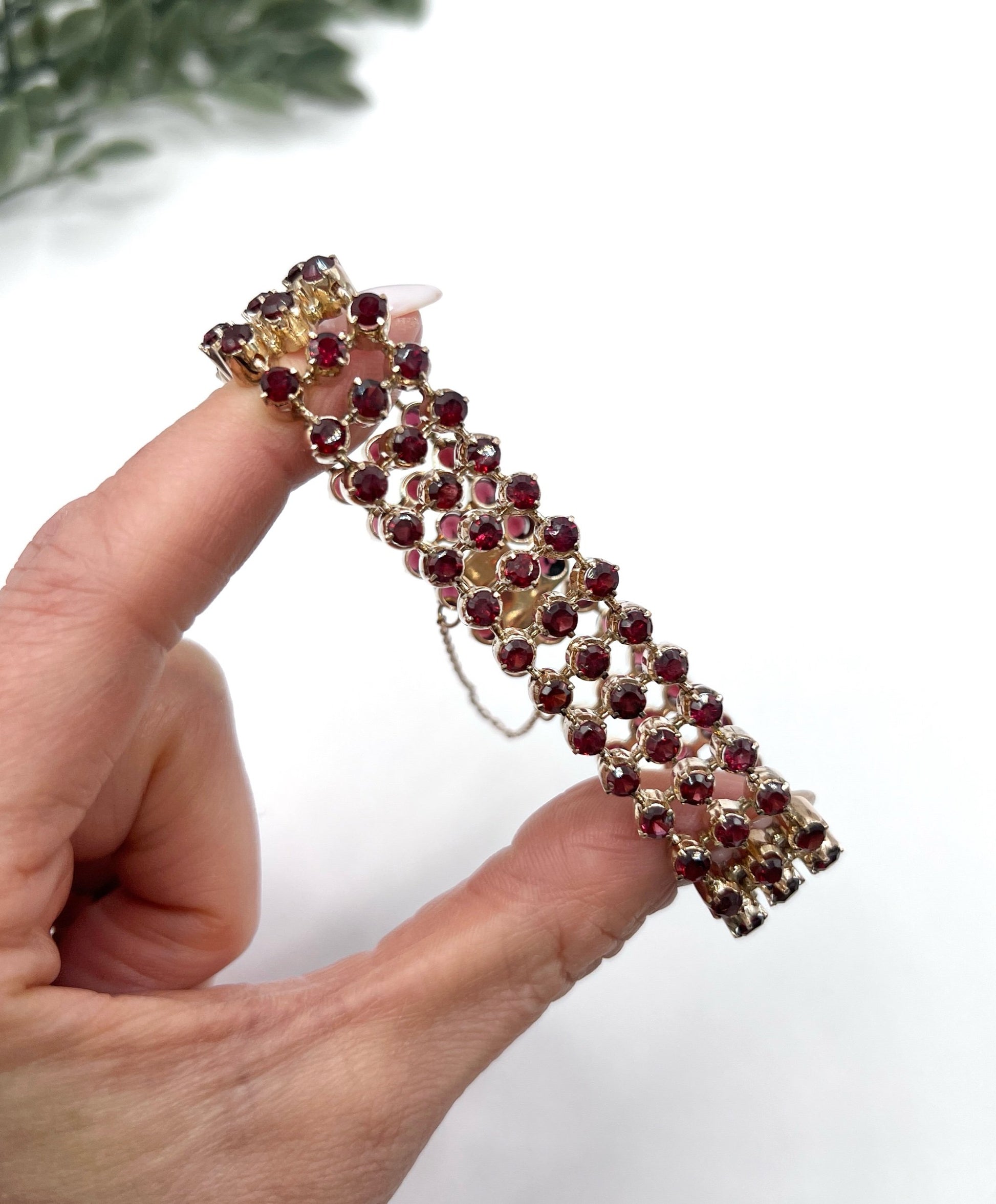 A triple row garnet bracelet in rose gold, held in a hand