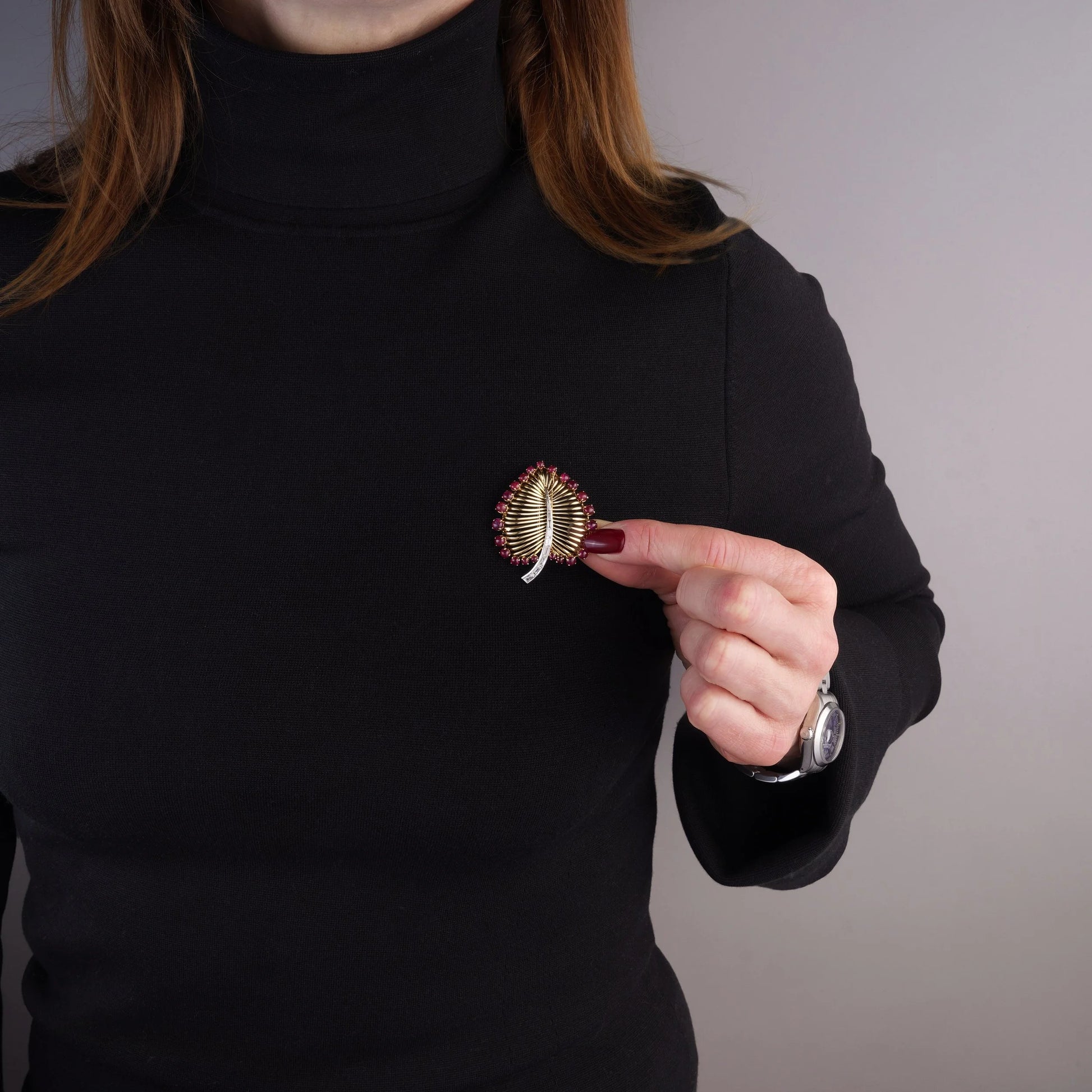 A gold and platinum leaf shaped brooch with baguette cut diamonds and cabochon cut rubies, modelled on a lady wearing a black top