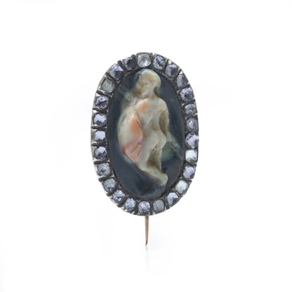 An oval cameo brooch depicting a nude figure, with diamonds around the border, on a white background