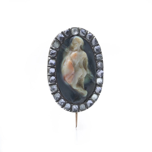 An oval cameo brooch depicting a nude figure, with diamonds around the border, on a white background