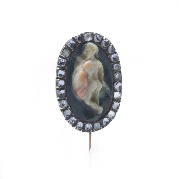 An oval cameo brooch depicting a nude figure, with diamonds around the border, on a white background