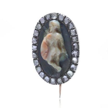 An oval cameo brooch depicting a nude figure, with diamonds around the border, on a white background