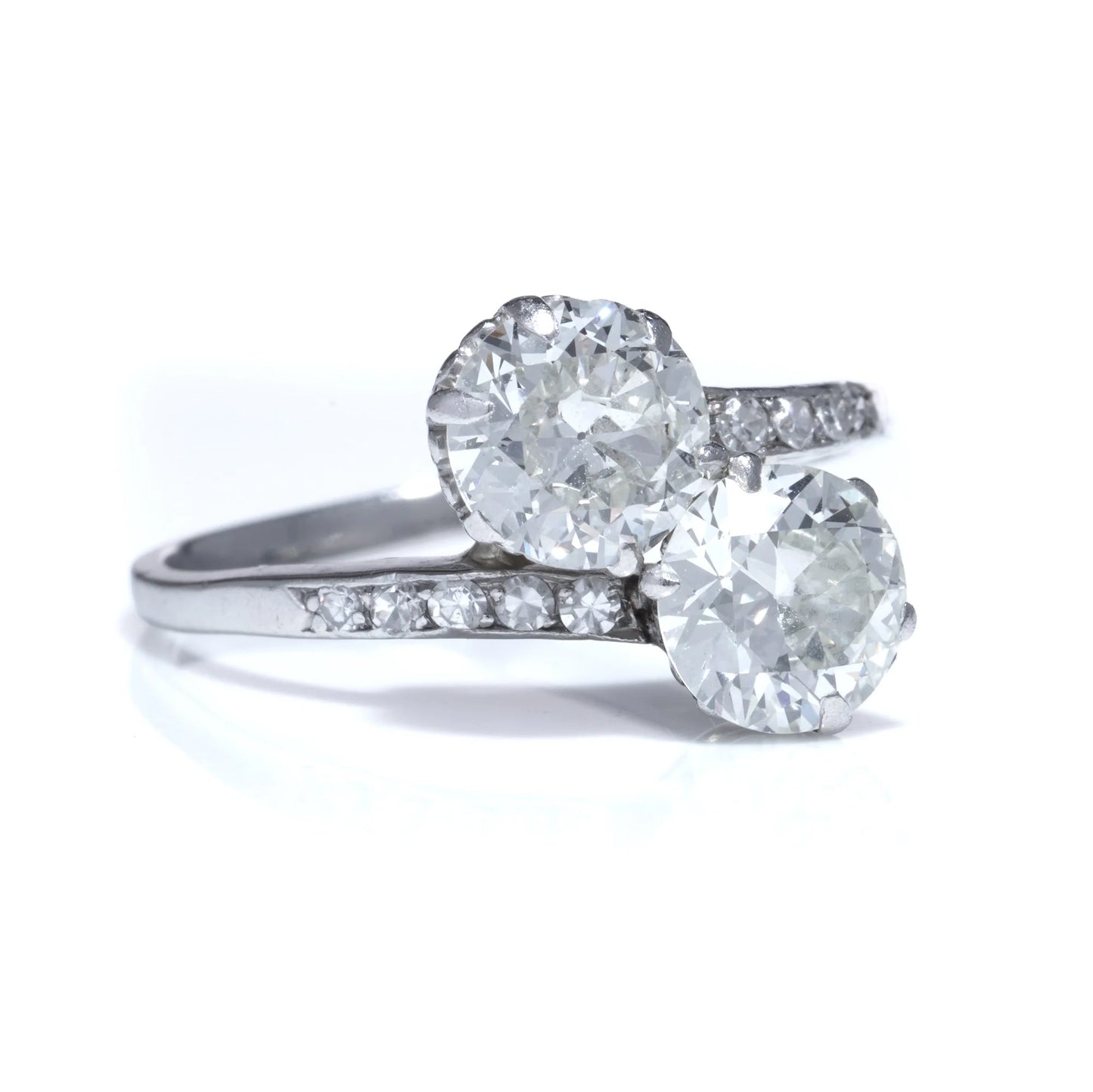A two stone diamond crossover ring in white gold with diamond shoulders, on a white background