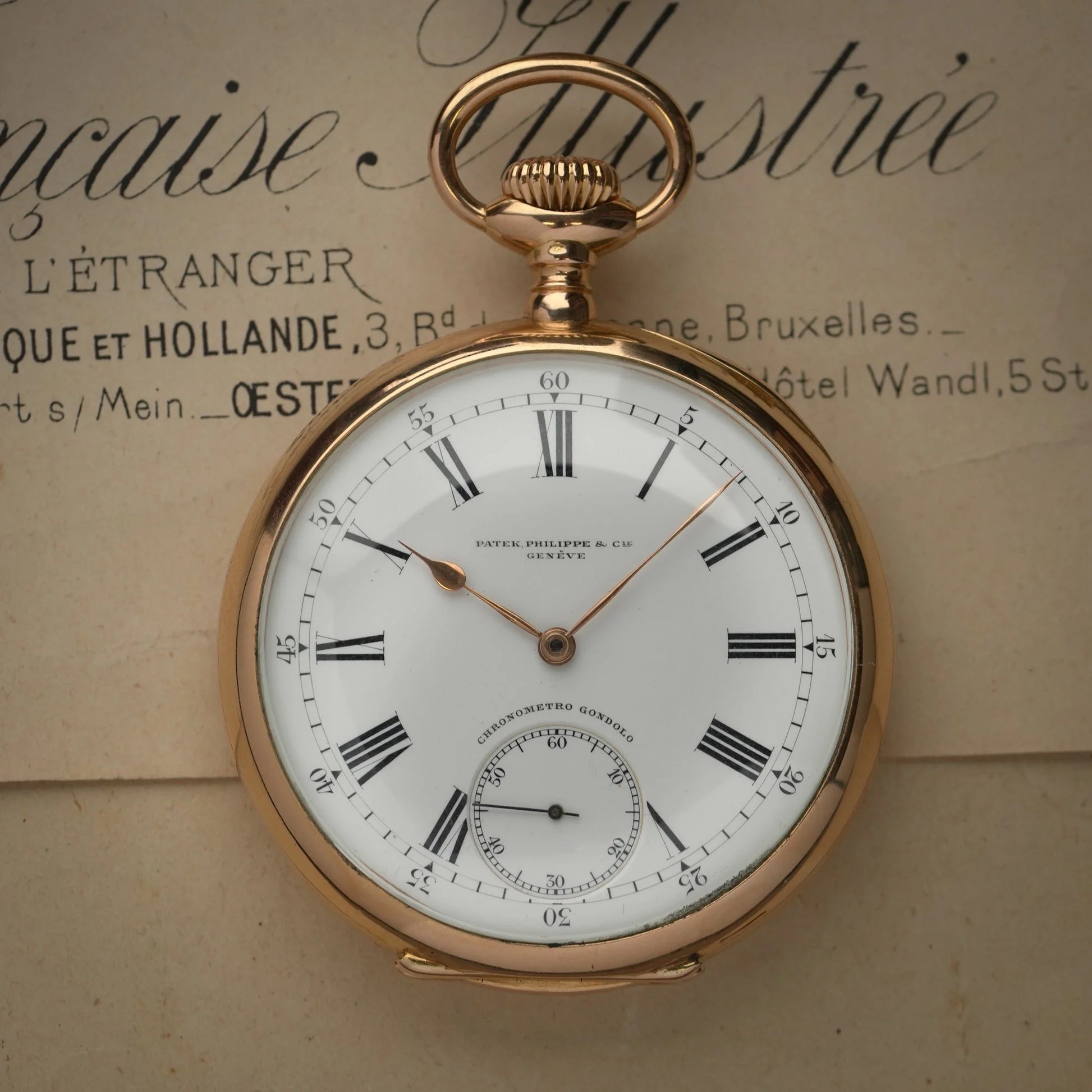 A yellow gold Patek Phillipe pocket watch with white dial and black Roman numerals, on a paper document 