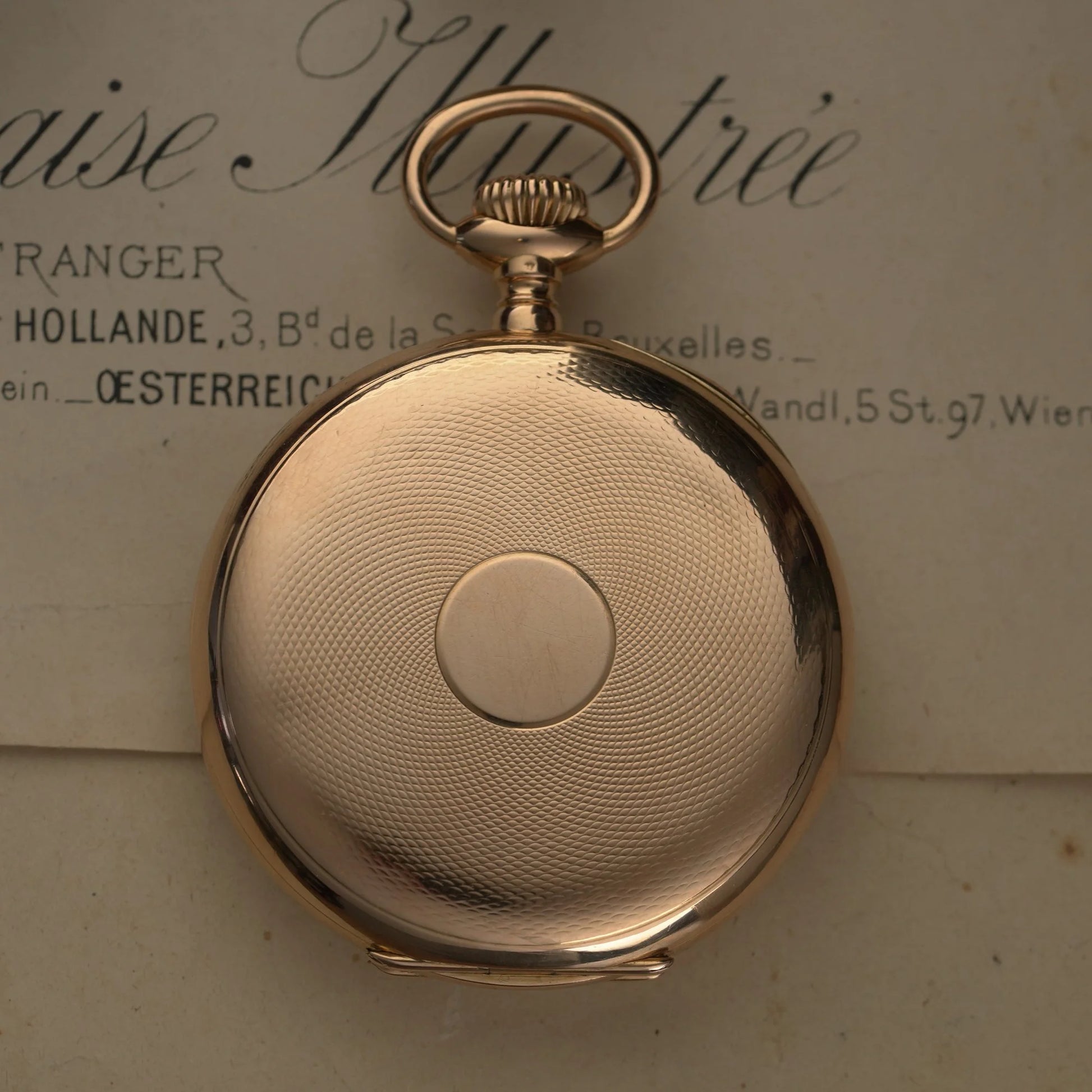 The back of a yellow gold pocket watch, on a paper document
