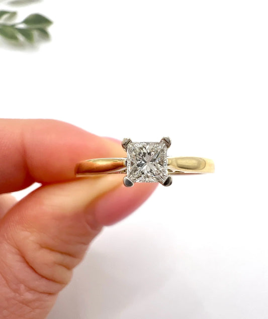 A solitaire princess cut diamond ring in yellow and white gold, held in a hand