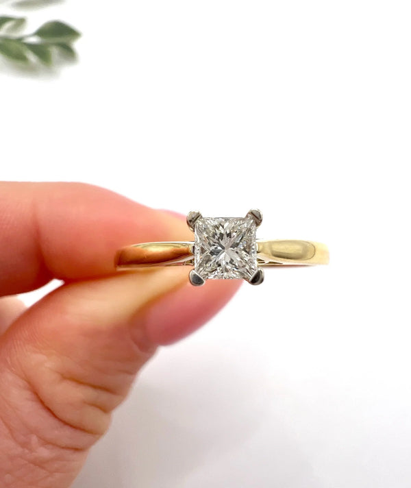 A solitaire princess cut diamond ring in yellow and white gold, held in a hand